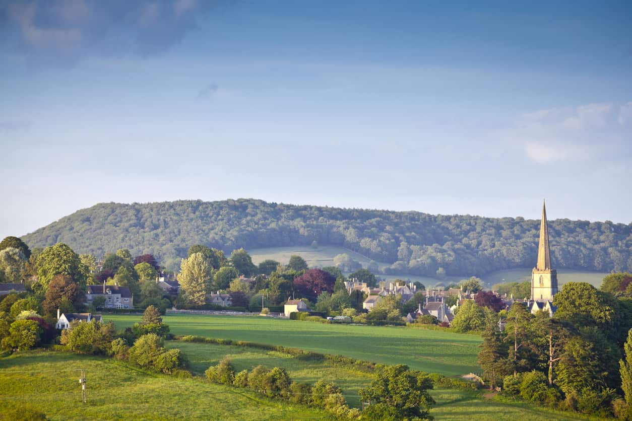 countryside landscape with houses and a steeple a mix between trees and hills