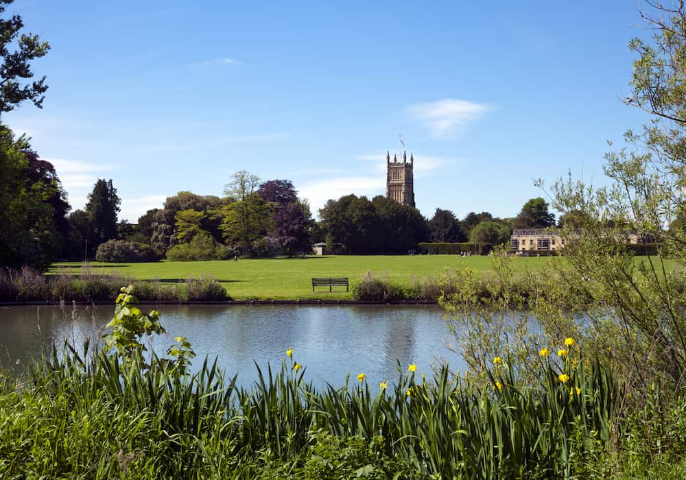 A big river in a park with the Cirencester church in the distance