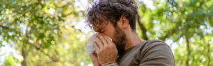 How Can You Tell if You Have an Alcohol Allergy - an image of a man with curly hair outside sneezing into a tissue