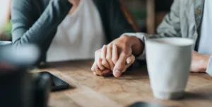 How to help an addict without enabling. An image of two people holding hands over a coffee